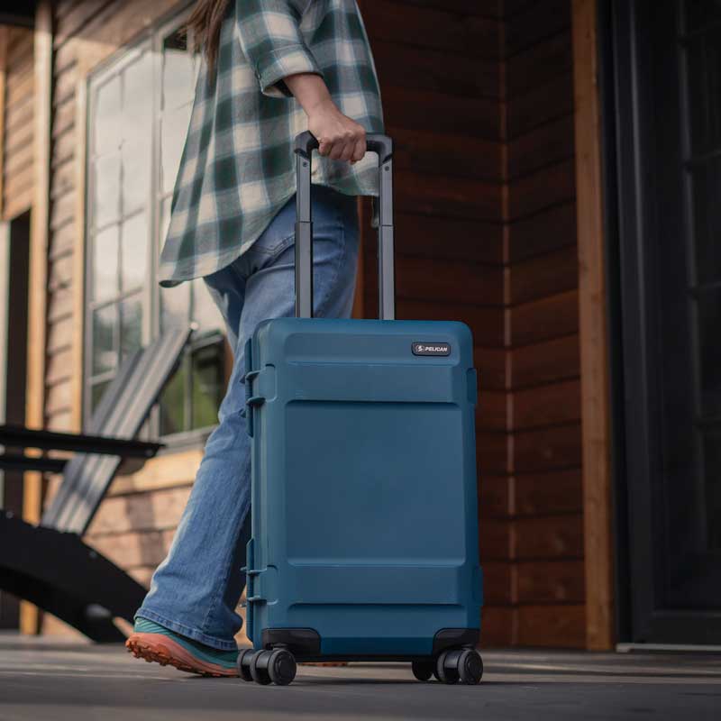 Person pulling a blue Peli ATX hard-shell carry-on suitcase with telescopic handle.