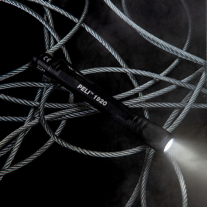 A black Peli 1920 LED Torch with a beam of light sat on top of an aesthetic grey rope on a black background