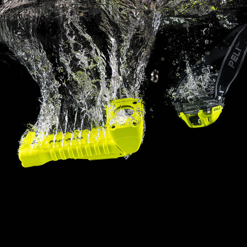 A yellow Peli 1415 Atex torch and a yellow Peli 2755 ATEX safety head torch submerged in water on a black background
