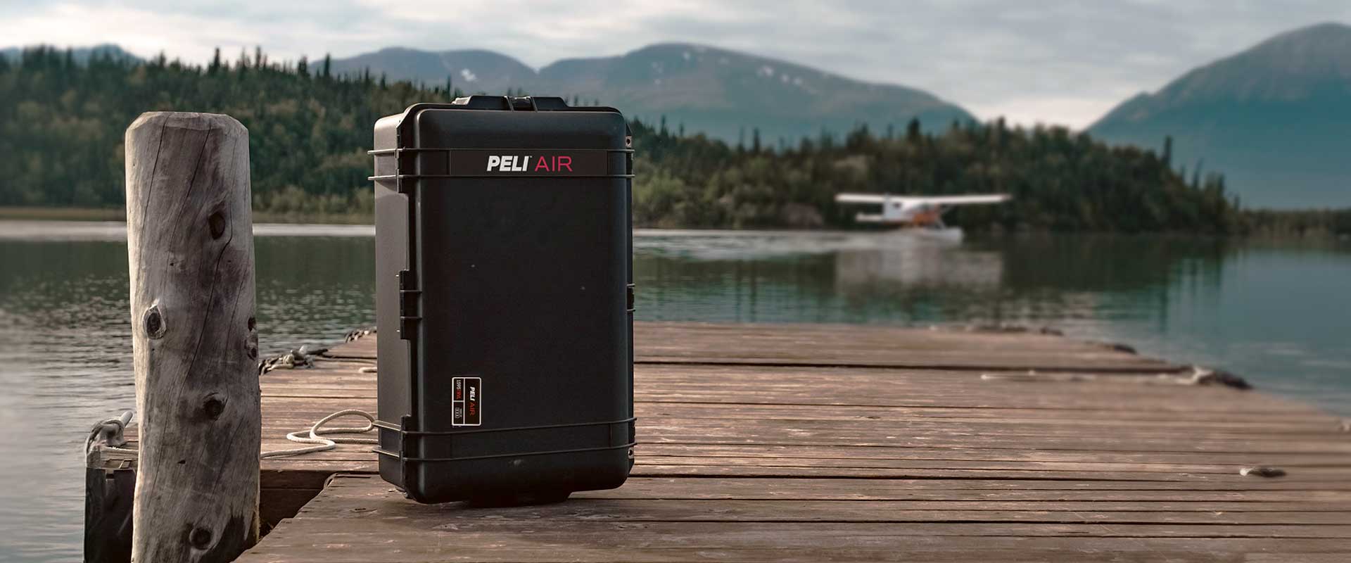 An image of a black Peli 1595 Air travel case on a pier, looking out towards the sea with an aeroplane in the background.