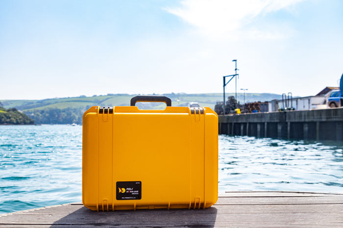 A yellow iM2600 PeliStorm case at a harbour with a view of the sea in the background.